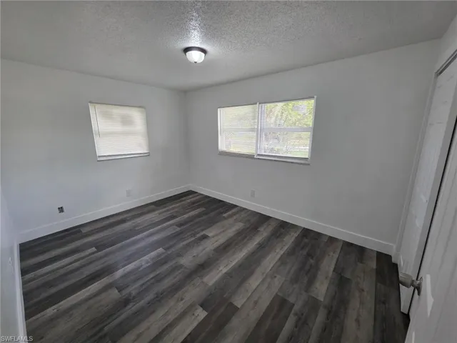 Unfurnished bedroom featuring a textured ceiling, a closet, and dark wood-style floors
