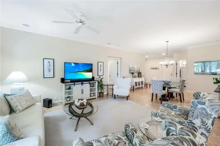 Tiled living area featuring ornamental molding, ceiling fan, and a chandelier