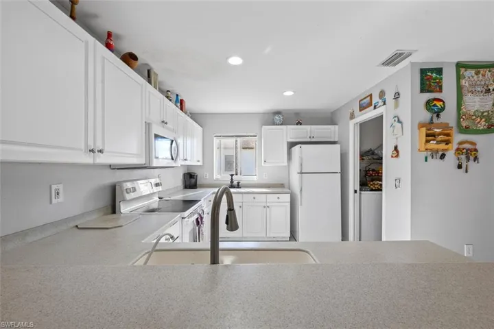 Kitchen with visible vents, light countertops, white cabinets, white appliances, and a sink