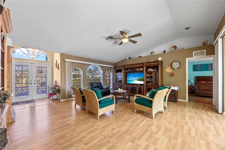 Living area with visible vents, vaulted ceiling, ceiling fan with notable chandelier, french doors, and light wood-style floors