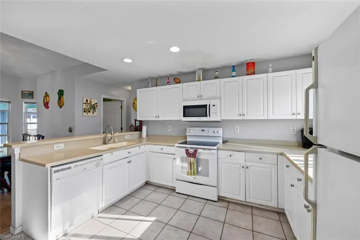 Kitchen with white cabinetry, white appliances, a peninsula, and a sink