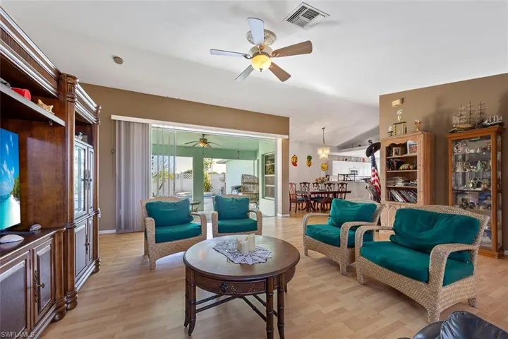 Living area with light wood-type flooring, visible vents, lofted ceiling, and a ceiling fan