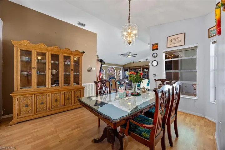 Dining area with visible vents, ceiling fan with notable chandelier, lofted ceiling, and light wood-style floors