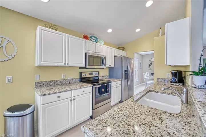 Kitchen with appliances with stainless steel finishes, light stone counters, vaulted ceiling, sink, and white cabinets