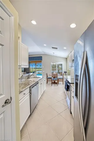 Kitchen with appliances with stainless steel finishes, sink, white cabinetry, hanging light fixtures, and lofted ceiling