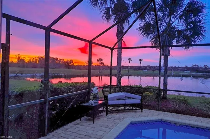 Pool at dusk with glass enclosure, a patio area, and a water view