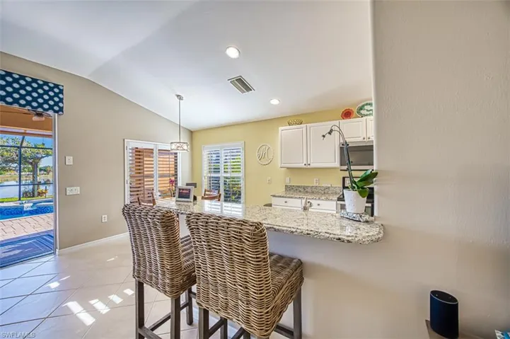 Kitchen featuring a kitchen bar, kitchen peninsula, white cabinetry, hanging light fixtures, and lofted ceiling
