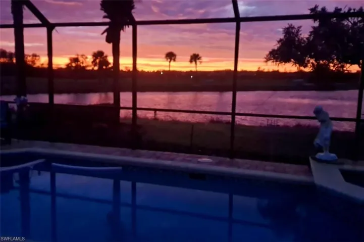Pool at dusk featuring a water view and glass enclosure