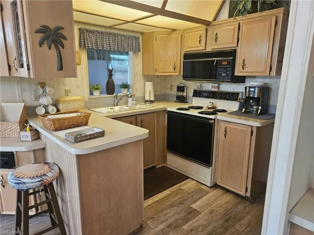 Kitchen with sink, wood-type flooring, light brown cabinets, white range with electric stovetop, and kitchen peninsula