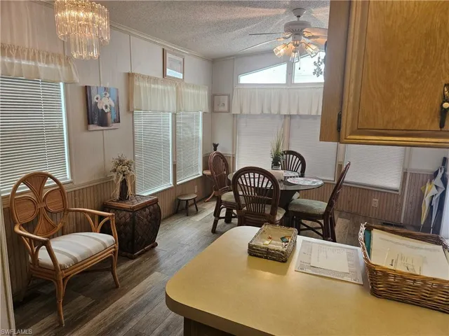 Dining space featuring a textured ceiling, ceiling fan with notable chandelier, and dark wood-type flooring