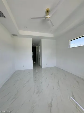Tiled empty room featuring ceiling fan and a raised ceiling