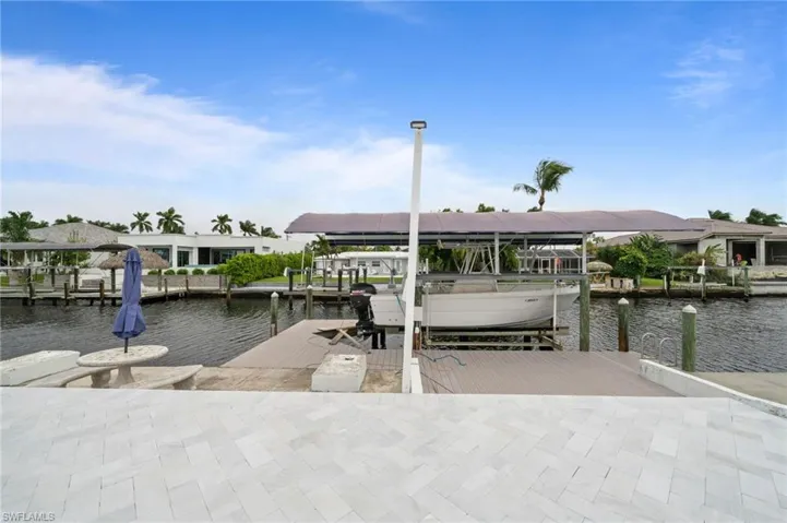 Waterfront dock featuring composite decking, a boat lift with a canopy cover, and a paved patio area