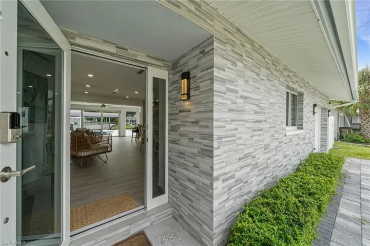 Exterior facade featuring multi-tonal stacked stone cladding, recessed ceiling lighting, wall-mounted exterior fixtures, and sliding glass entry doors