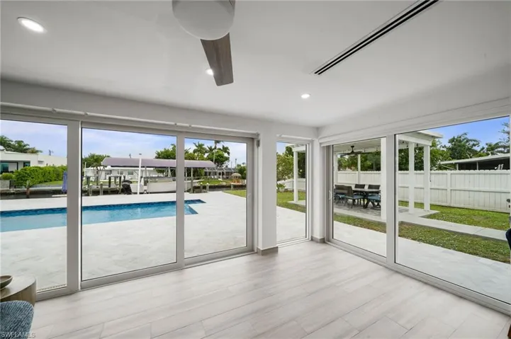 Interior space featuring light-toned wood-finish flooring, recessed lighting, ceiling fan, and floor-to-ceiling sliding glass doors opening to a pool, patio, and canal-front exterior