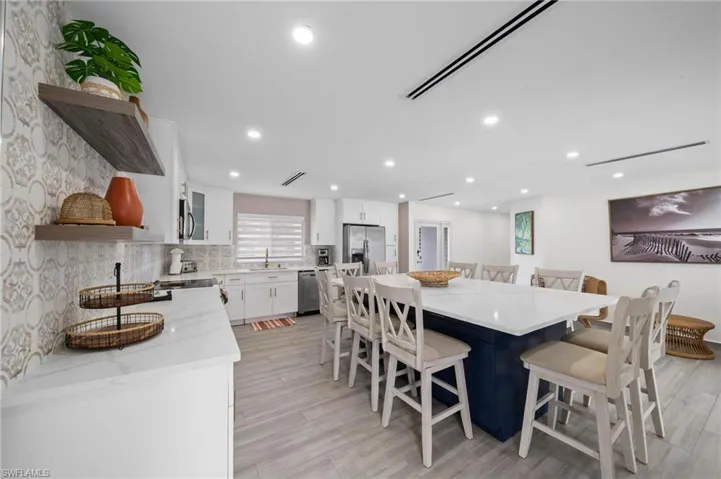 Kitchen featuring white cabinetry, a dark blue central island with a stone-finish countertop, patterned tile backsplash, recessed lighting, and wood-finish flooring