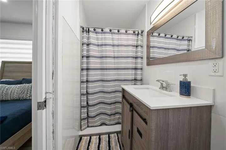 Bathroom vanity with wood-finish cabinetry, white countertop, integrated sink, metal hardware, and framed wall-mounted mirror
