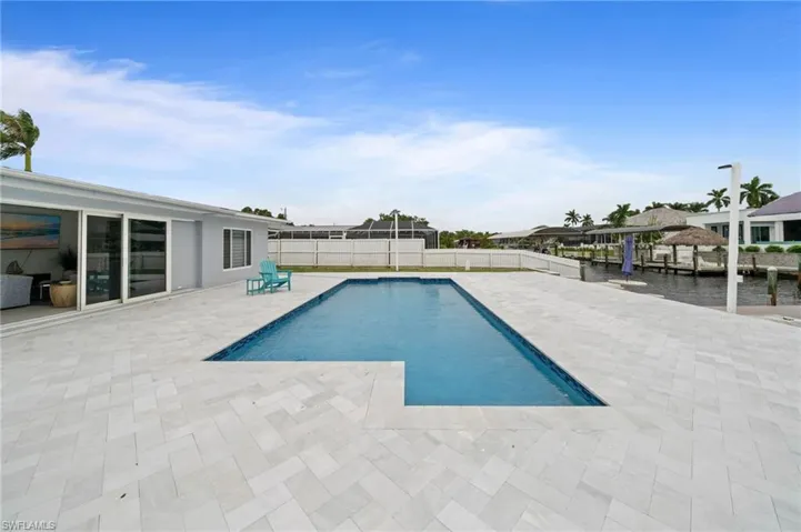 In-ground swimming pool with a stone paver deck, white privacy fencing, and direct water frontage