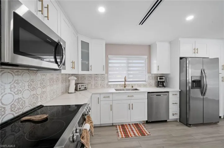 Kitchen featuring white cabinetry with brass-finish hardware, patterned tile backsplash, stainless steel appliances, solid-surface countertops, and wood-finish flooring