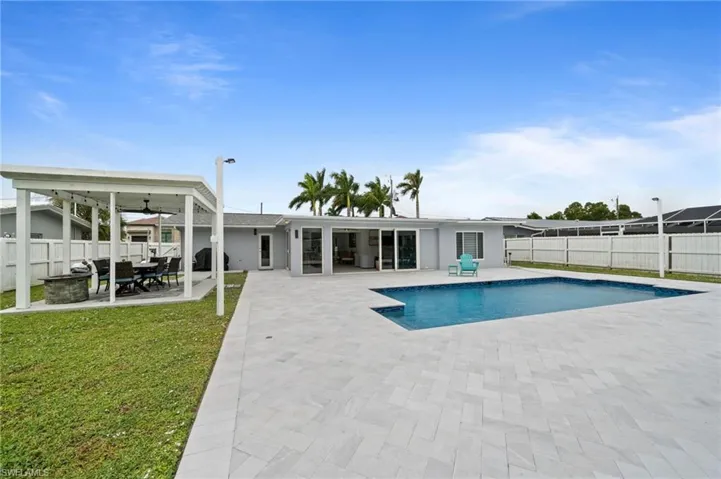 Expansive outdoor area featuring a swimming pool, herringbone-patterned stone pavers, a white pergola, and perimeter vinyl fencing