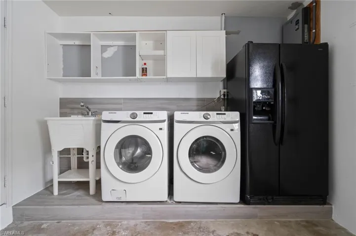 Utility area featuring white shaker-style wall cabinets, a utility sink with a chrome faucet, and tile-finish flooring