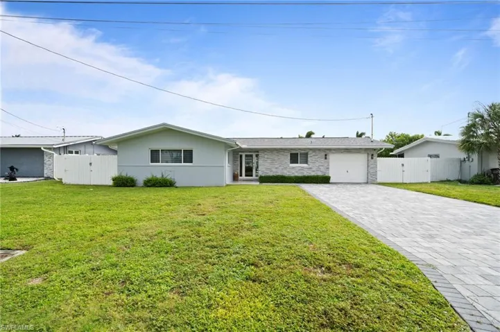 Single-story residence featuring a mixed stone and painted exterior, a paved driveway, and white perimeter privacy fencing