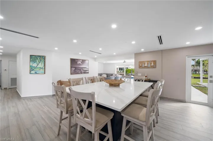 Large kitchen island featuring a white surface with grey veining, a dark-toned base, wood-finish flooring, recessed lighting, and a glass-paneled exterior door