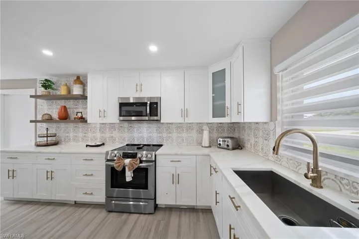 Kitchen featuring white Shaker-style cabinetry, patterned tile backsplash, quartz countertops, stainless steel appliances, and wood-finish flooring