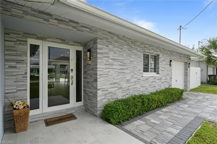 Exterior facade featuring stacked stone veneer, covered entryway, glass-paneled front door with side lights, paver driveway, and mounted exterior lighting