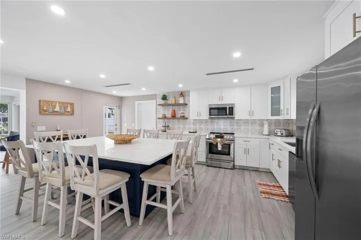 Kitchen featuring a center island with a stone-surface countertop, white cabinetry, stainless steel appliances, patterned tile backsplash, and wood-finish flooring