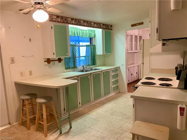 Kitchen featuring a breakfast bar area, white stove, sink, green cabinets, and ceiling fan