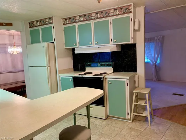 Kitchen with decorative backsplash, a notable chandelier, light colored carpet, and white appliances