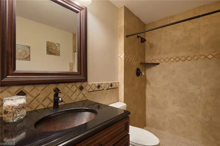Bathroom featuring a tile shower, tasteful backsplash, a textured ceiling, toilet, and vanity