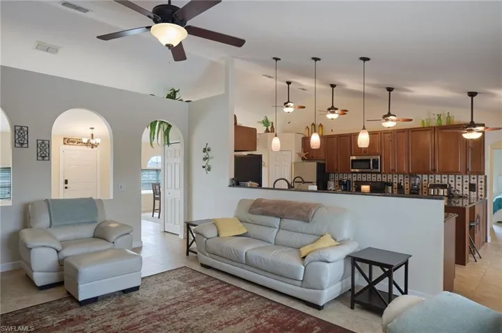 Living room featuring ceiling fan with notable chandelier, lofted ceiling, and light tile patterned flooring