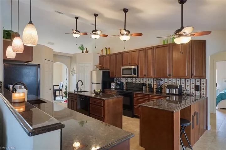 Kitchen featuring black appliances, sink, vaulted ceiling, an island with sink, and tasteful backsplash