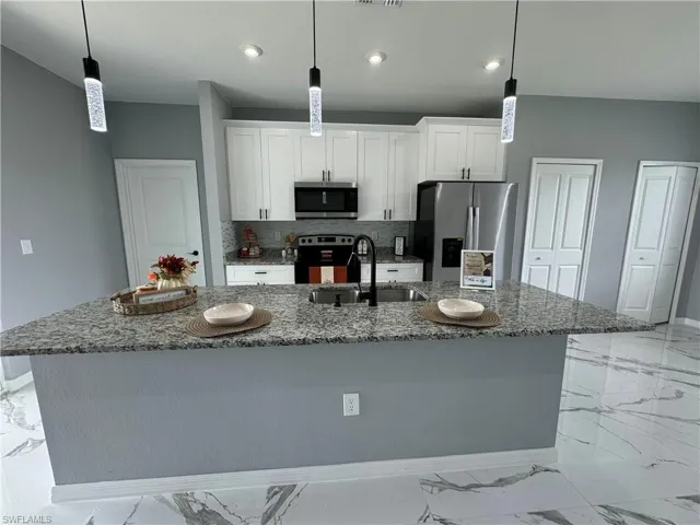 Kitchen featuring a kitchen island with sink, stainless steel appliances, light tile patterned floors, and white cabinetry