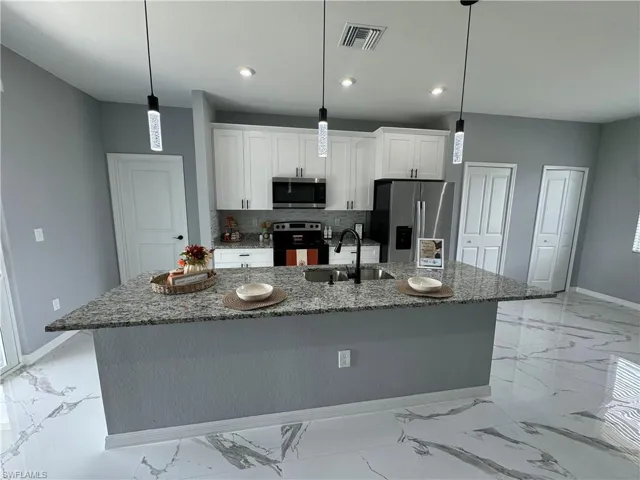 Kitchen featuring light tile patterned flooring, appliances with stainless steel finishes, sink, and an island with sink