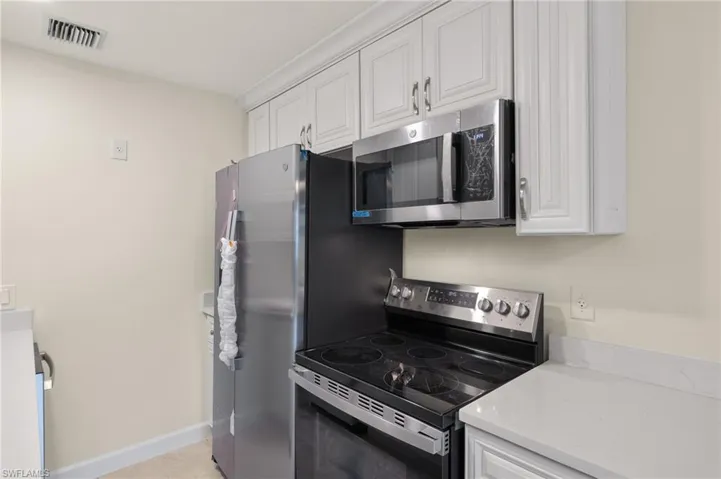 Kitchen with stainless steel appliances, light tile patterned flooring, and white cabinets