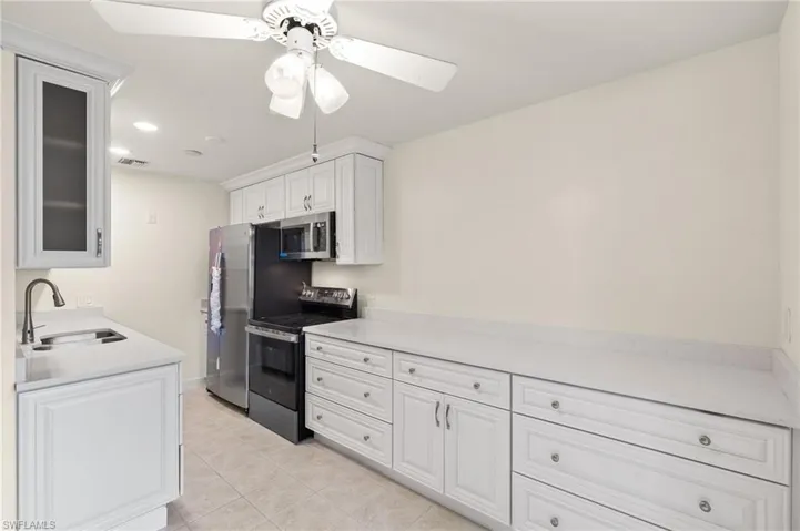 Kitchen with light tile patterned flooring, sink, white cabinetry, ceiling fan, and stainless steel appliances