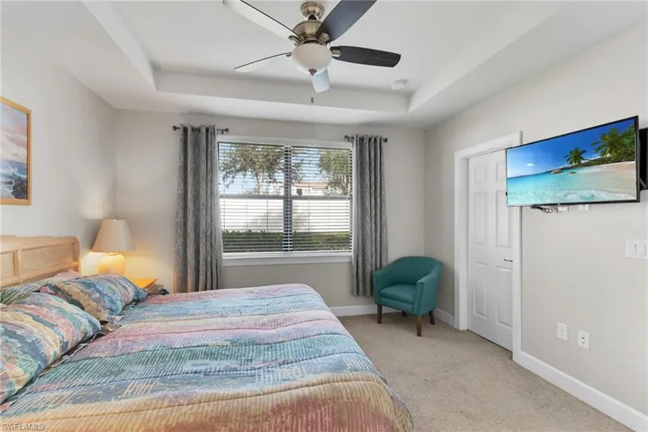 Bedroom featuring a raised ceiling, light colored carpet, and a ceiling fan