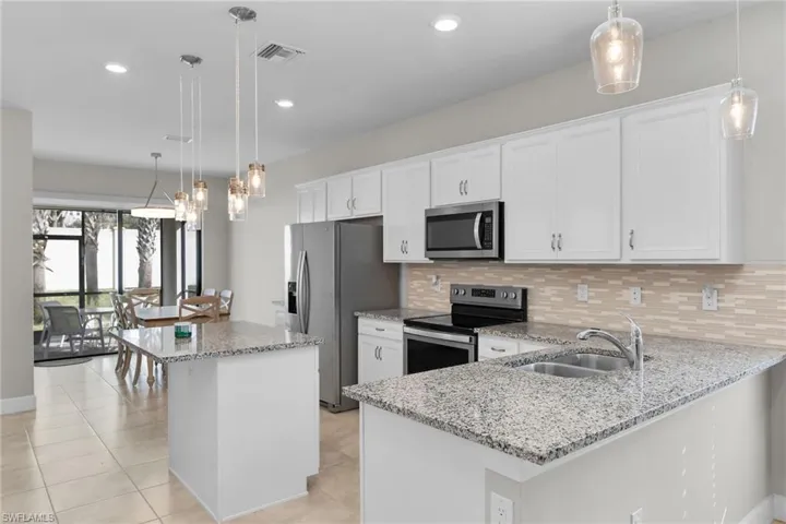 Kitchen featuring hanging light fixtures, light stone countertops, stainless steel appliances, decorative backsplash, and white cabinets