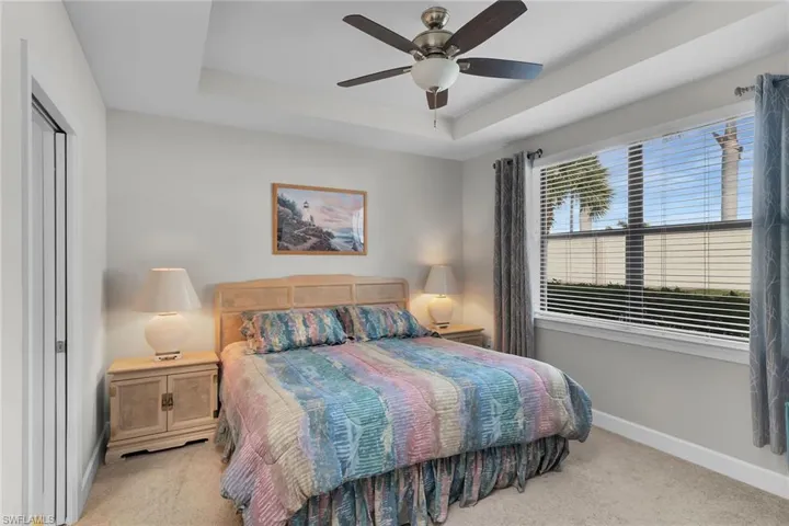 Bedroom with a raised ceiling, a ceiling fan, and light carpet