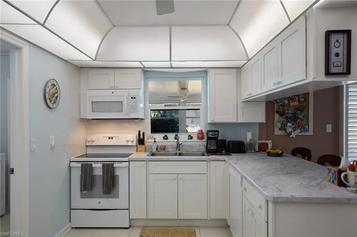 Kitchen with white appliances, light countertops, white cabinets, a peninsula, and light tile patterned floors