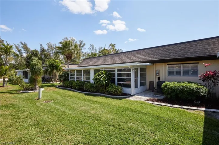 Back of house with a shingled roof, a yard, a sunroom, and stucco siding