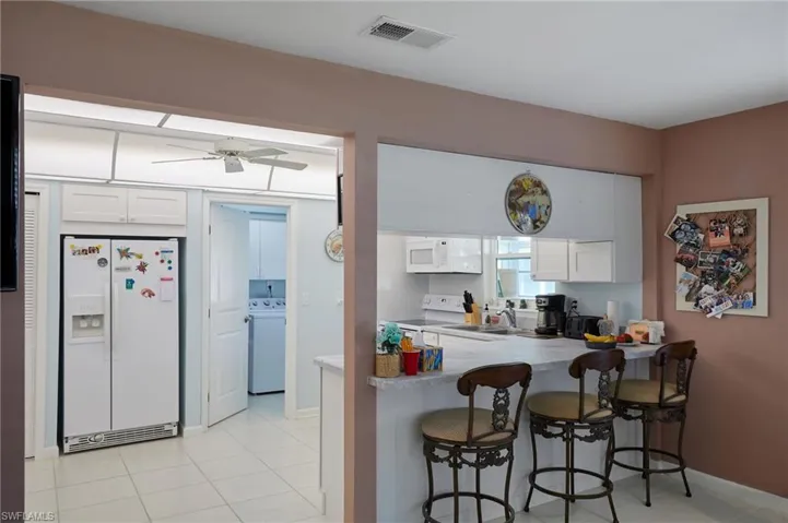 Kitchen featuring white appliances, white cabinets, a kitchen breakfast bar, washer / clothes dryer, and light countertops