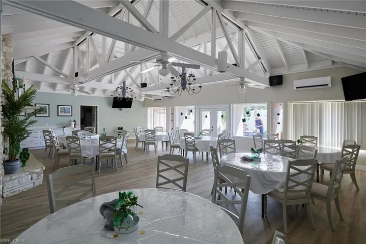 Dining area with high vaulted ceiling, wood finished floors, an AC wall unit, beam ceiling, and ceiling fan