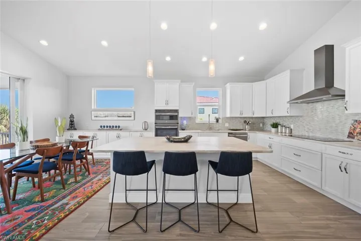 Kitchen featuring white cabinetry, a center island, wall chimney range hood, vaulted ceiling, and appliances with stainless steel finishes