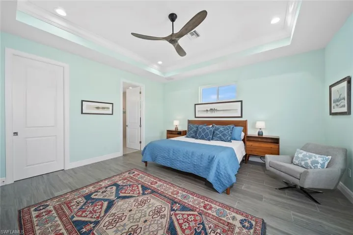 Bedroom with hardwood / wood-style floors, a tray ceiling, and ceiling fan