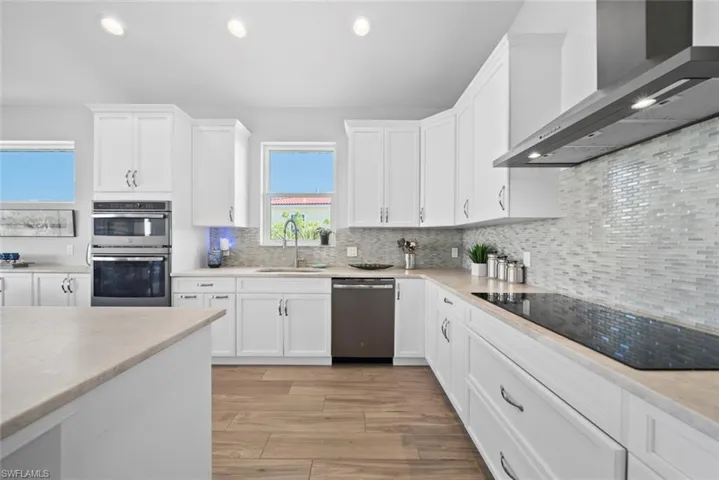 Kitchen featuring light wood-type flooring, wall chimney exhaust hood, stainless steel appliances, sink, and white cabinets