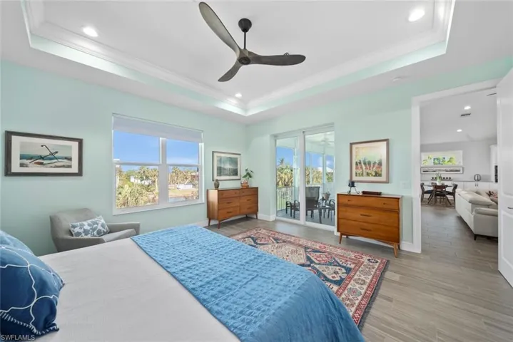 Bedroom featuring access to exterior, ornamental molding, a raised ceiling, ceiling fan, and light hardwood / wood-style flooring