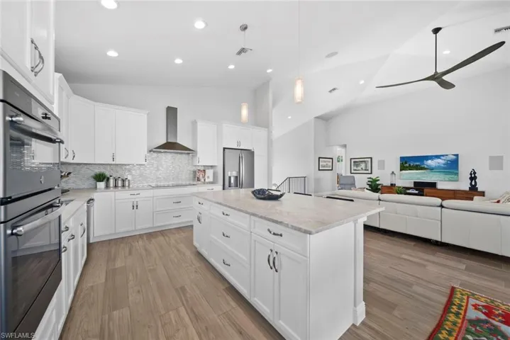 Kitchen with a center island, wall chimney exhaust hood, pendant lighting, white cabinets, and black appliances